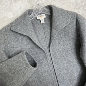 Puede incluir: Chaqueta de lana gris claro con cuello con solapas y mangas largas. La chaqueta está colgada de una percha de plástico transparente. La etiqueta dice "Talbots".