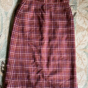 May include: A knee-length skirt in a plaid pattern. The skirt features a brown, burgundy, and white checkered design. The skirt has a button closure and a small slit at the back. The fabric appears to be a woven material.