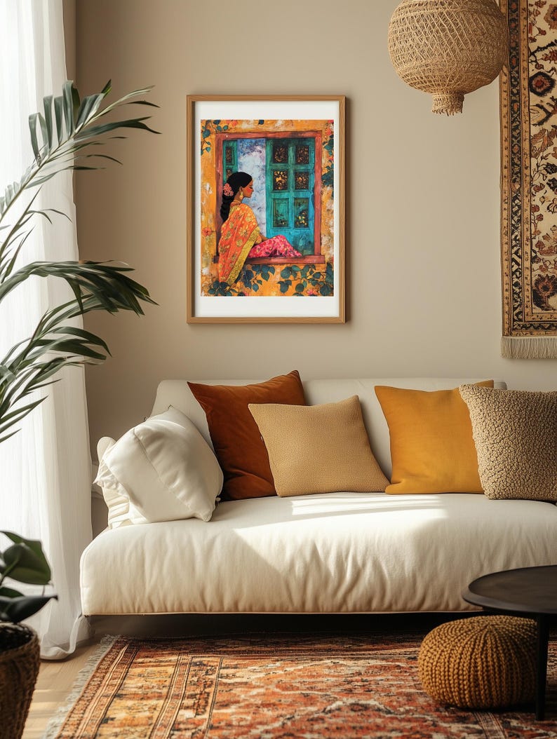 Peut inclure: Une impression encadr&eacute;e d'une femme en sari color&eacute; assise pr&egrave;s d'une fen&ecirc;tre avec une porte turquoise. La fen&ecirc;tre est entour&eacute;e de fleurs et de feuilles jaunes. L'impression est accroch&eacute;e &agrave; un mur beige au-dessus d'un canap&eacute; blanc avec des coussins.