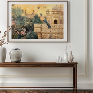 Op de afbeelding: Een ingelijst aquarel schilderij van een vogel die op een muur zit met uitzicht op een gouden gebouw met een koepel. Het gebouw is omgeven door weelderig groen en een roze bloeiende boom. Het schilderij hangt aan een witte muur boven een houten consoletafel met twee vazen en een decoratief object.