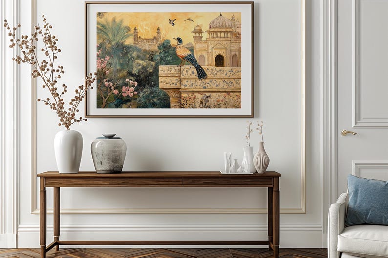 Op de afbeelding: Een ingelijst aquarel schilderij van een vogel die op een muur zit met uitzicht op een gouden gebouw met een koepel. Het gebouw is omgeven door weelderig groen en een roze bloeiende boom. Het schilderij hangt aan een witte muur boven een houten consoletafel met twee vazen en een decoratief object.