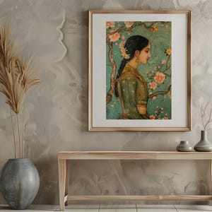 K&ouml;nnte beinhalten: Ein gerahmtes Gem&auml;lde einer Frau in einem gr&uuml;nen Kleid, die vor einem bl&uuml;henden Baum steht. Das Gem&auml;lde ist vor einer hellbraunen Wand platziert, mit einer Vase mit getrockneten Blumen und einer Holzbank im Vordergrund.