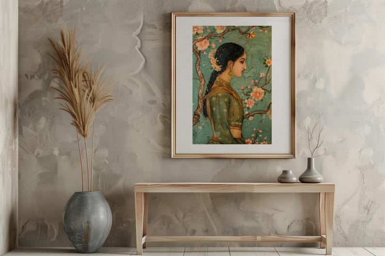 K&ouml;nnte beinhalten: Ein gerahmtes Gem&auml;lde einer Frau in einem gr&uuml;nen Kleid, die vor einem bl&uuml;henden Baum steht. Das Gem&auml;lde ist vor einer hellbraunen Wand platziert, mit einer Vase mit getrockneten Blumen und einer Holzbank im Vordergrund.