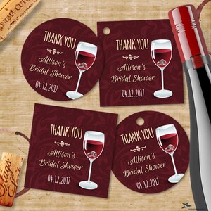 Puede incluir: Cuatro etiquetas de regalo para botellas de vino con fondo burdeos y texto dorado. Las etiquetas muestran una copa de vino tinto con dos anillos dorados en su interior. El texto en las etiquetas dice "Gracias", "Ducha nupcial de Allison" y "04.12.2017".