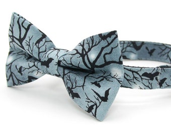 May include: A blue cat collar with a black and white bat and tree pattern bow tie and a silver bell.