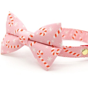 Può includere: Collare per gatto rosa con un papillon con motivo a bastoncino di zucchero e fiocco di neve. Il collare ha un campanello dorato.