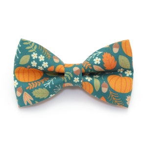 Puede incluir: Una pajarita azul verdosa con un estampado de otoño con calabazas, hojas, bellotas y flores blancas.
