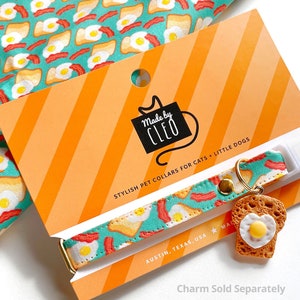 K&ouml;nnte beinhalten: Ein t&uuml;rkisfarbenes und wei&szlig;es Halsband f&uuml;r Haustiere mit einem Fr&uuml;hst&uuml;cks-Motiv aus Eiern, Speck und Toast. Das Halsband wird von Cleo hergestellt und ist f&uuml;r Katzen und kleine Hunde geeignet. Der Text "Made by Cleo" und "Stylish Pet Collars for Cats + Little Dogs" befindet sich auf der Verpackung. Der Text "Austin, Texas, USA" befindet sich ebenfalls auf der Verpackung. Der Anh&auml;nger wird separat verkauft.