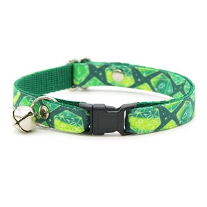 May include: Green cat collar with a dice pattern and a silver bell. The collar has a black plastic buckle.