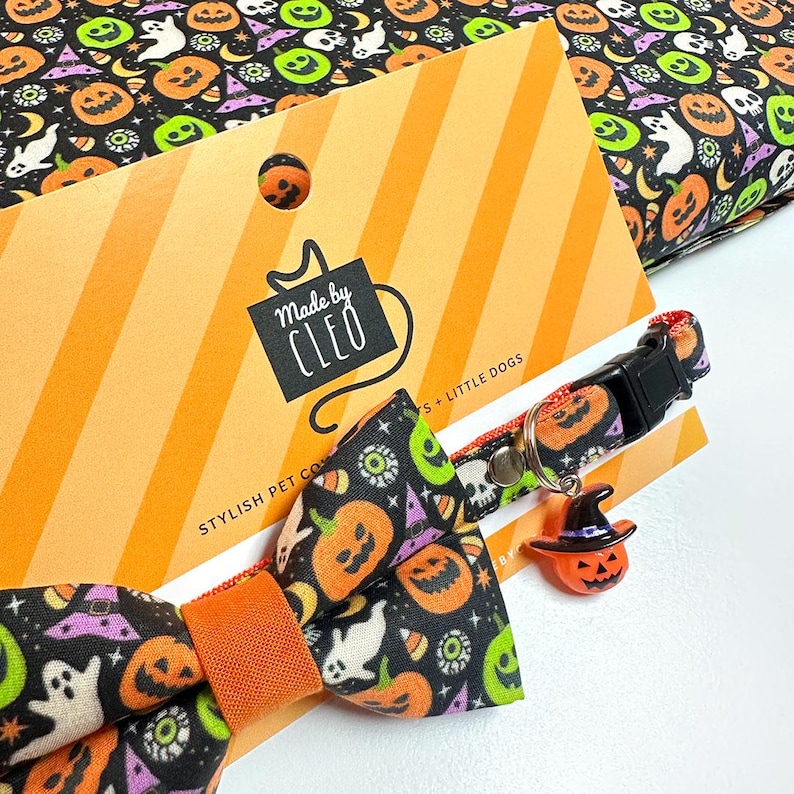 May include: A black pet collar with a bow tie featuring a Halloween pattern of orange pumpkins, white ghosts, green skulls, and purple witch hats. The collar includes a black plastic buckle, a metal D-ring, and a small orange pumpkin charm with a hat.