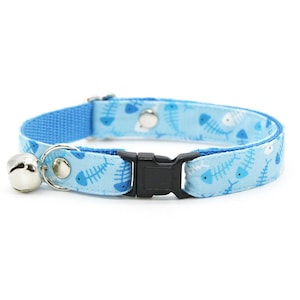May include: Light blue cat collar with a fishbone pattern in shades of blue and white. The collar has a black plastic buckle, a silver bell, and a matching blue fabric backing.