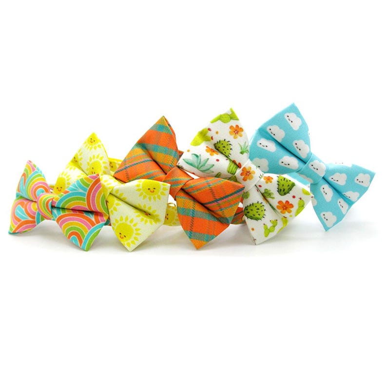 May include: A collection of six colorful bow ties with various patterns. Designs include rainbows, sunshine, plaid, cacti, and clouds. The bow ties are made of fabric and are arranged in a row against a white background.