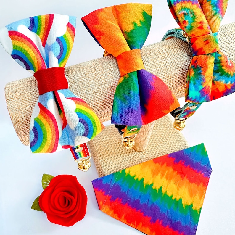Może przedstawiać: Trzy kolorowe obroże dla psa w stylu tie-dye z wzorami tęczy. Obroże są prezentowane na brązowym stojaku. Jedna obroża ma wz&oacute;r tęczy i chmur, druga ma wz&oacute;r tie-dye, a trzecia ma wz&oacute;r tęczy i chmur.