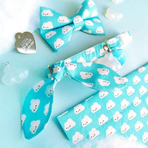 May include: A pet collar, bow tie, and matching fabric in a light blue color with a repeating pattern of smiling white clouds. A silver heart-shaped tag and a cloud-shaped charm are also included. The tag has the name "LUNA" and a phone number.