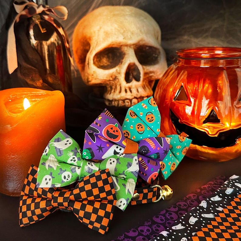 May include: Three Halloween-themed bow ties with different patterns: ghosts, pumpkins, and candy corn. The bow ties are on a black surface with a skull, a pumpkin, and a candle in the background.