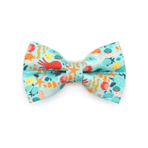 May include: A turquoise blue bow tie with a colorful sea life pattern. The pattern includes seahorses, starfish, jellyfish, and an octopus.