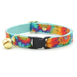 Może przedstawiać: Turkusowy niebieski kotek z wzorem tie-dye w odcieniach pomarańczowego, ż&oacute;łtego, czerwonego i fioletowego. Kołnierz ma czarną plastikową klamrę i złoty dzwonek.