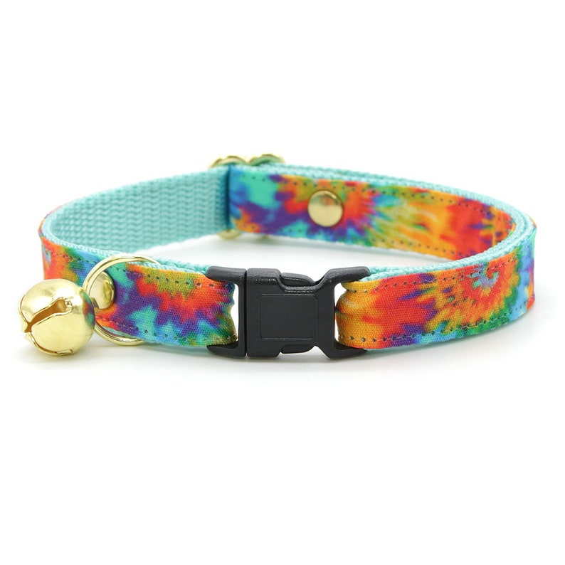 Może przedstawiać: Turkusowy niebieski kotek z wzorem tie-dye w odcieniach pomarańczowego, ż&oacute;łtego, czerwonego i fioletowego. Kołnierz ma czarną plastikową klamrę i złoty dzwonek.