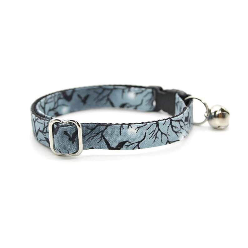 May include: A blue and black cat collar with a silver bell and a silver buckle. The collar has a pattern of bats and trees.