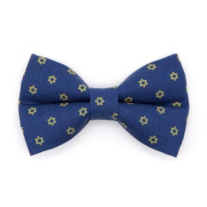 May include: A navy blue bow tie with a repeating pattern of yellow six-pointed stars. The bow tie is a classic shape, with a pre-tied knot and adjustable neckband. The fabric has a subtle sheen.