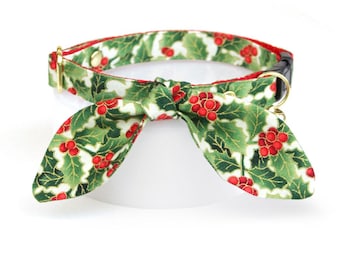 May include: A green and red Christmas holly print cat collar with a gold buckle and a bow tie.