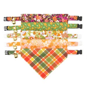 May include: Set of six colourful cat collars with bell charms. The collars feature various floral and plaid patterns in shades of orange, green and brown.