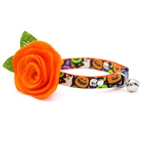 Puede incluir: Un collar para gatos con tem&aacute;tica de Halloween, con un patr&oacute;n negro de calabazas, fantasmas y calaveras. Cuenta con una rosa de fieltro naranja y una campana plateada.
