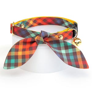 May include: A plaid cat collar with a yellow trim and a matching bow tie. The collar has a bell attached.