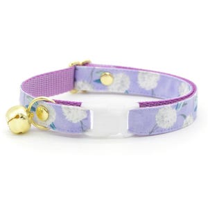 May include: A purple and white floral cat collar with a gold bell and a white safety buckle.