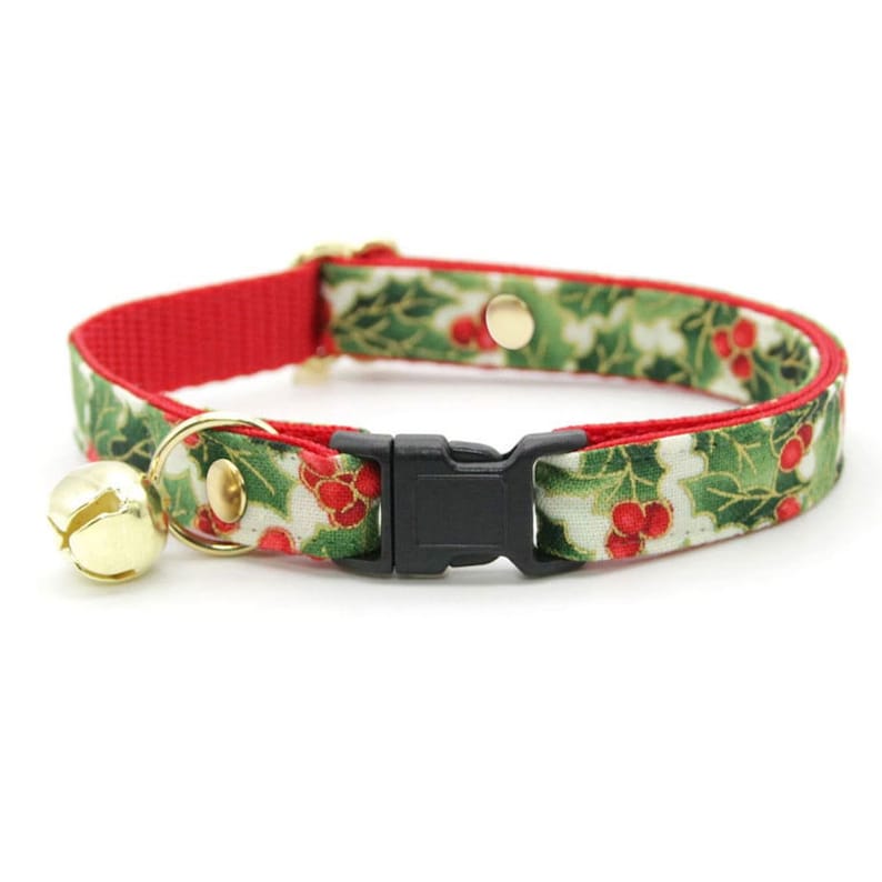 May include: A red and green Christmas-themed cat collar with a bell. The collar has a holly and berry pattern and a black plastic buckle.