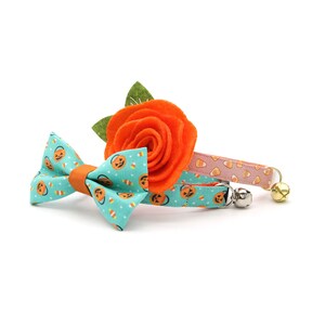 May include: A turquoise blue bow tie with a pattern of orange jack-o'-lanterns and candy corn, paired with a pink and orange collar with a candy corn pattern and a silver bell.