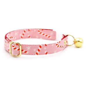 May include: Pink cat collar with a red and white candy cane pattern and a gold bell.