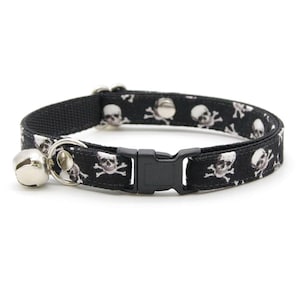 May include: Black cat collar with a skull and crossbones pattern. The collar has a safety buckle and a bell.