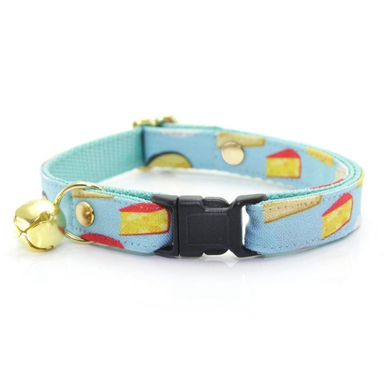 May include: A light blue cat collar with a pattern of yellow and red cheese slices. The collar has a black buckle and a gold bell.