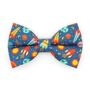 May include: A blue bow tie with a space-themed pattern featuring rockets, planets, stars, and suns.