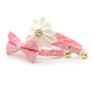 May include: Pink snowflake patterned cat collar with a matching bow tie and a white flower with a rhinestone center.