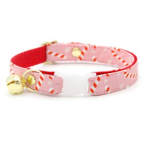 May include: Pink cat collar with a red and white candy cane pattern, a gold bell, and a white plastic safety buckle.
