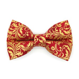 Könnte beinhalten: Eine rote Fliege mit goldenem Blumenmuster. Die Fliege ist zentriert und hat ein symmetrisches Design. Das goldene Muster ist ein sich wiederholendes Design aus wirbelnden Blättern und Ranken.