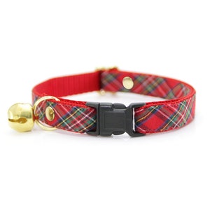 May include: Red cat collar with a festive plaid pattern in green, yellow, and white. The collar features a gold-colored bell and buckle, and a black plastic clasp. A stylish accessory for your feline friend.