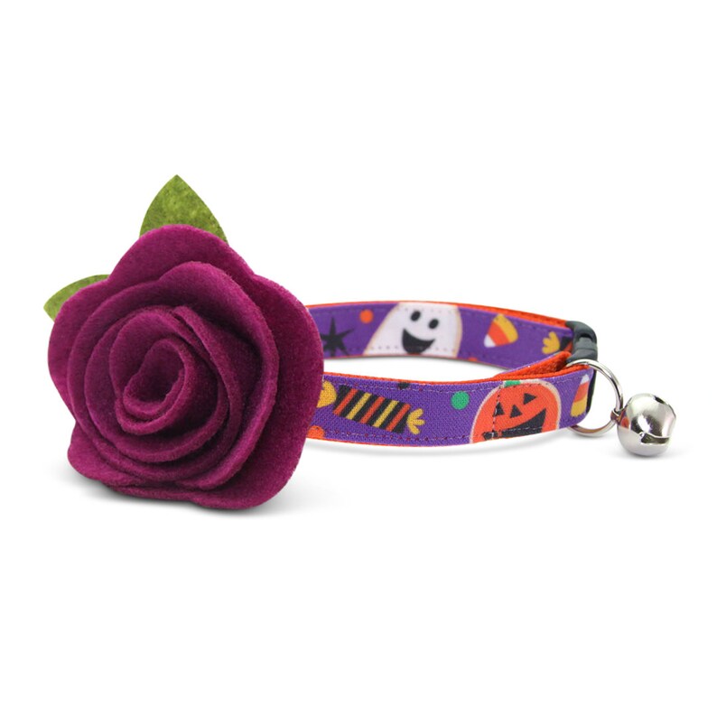 May include: Purple felt flower cat collar with a Halloween themed print featuring ghosts, candy corn, and pumpkins. The collar has a bell.