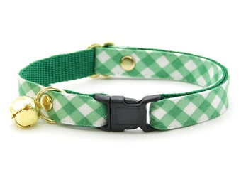 Könnte beinhalten: Grünes und weißes Gingham-Katzenhalsband mit einer goldenen Glocke und einer schwarzen Kunststoffschnalle.