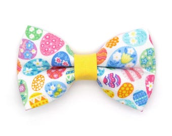 May include: A white bow tie with a yellow center and a pattern of colorful Easter eggs.