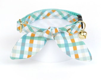 May include: A turquoise and orange plaid cat collar with a bow tie and a bell.