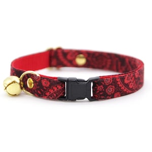 May include: Red cat collar with a black paisley pattern, a gold-colored bell, and a black plastic buckle. The collar is designed for cats and features a safety breakaway buckle.