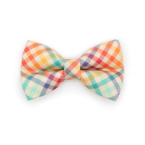 Puede incluir: Una pajarita de cuadros de colores con fondo beige claro. La pajarita presenta una variedad de colores, incluyendo naranja, rojo, amarillo, verde y azul.