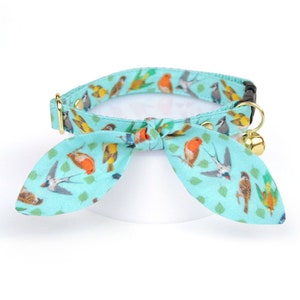 Può includere: Un collare per gatti turchese con fiocco, decorato con uccelli colorati e foglie verdi. Il collare ha un campanello dorato e accessori in metallo dorato.