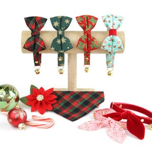 May include: A set of five festive Christmas-themed cat collars and bandanas. The collars feature a variety of patterns, including plaid, snowflakes, holly, and a snowman design. The bandanas are red and green plaid and red velvet with a pink and white candy cane pattern.