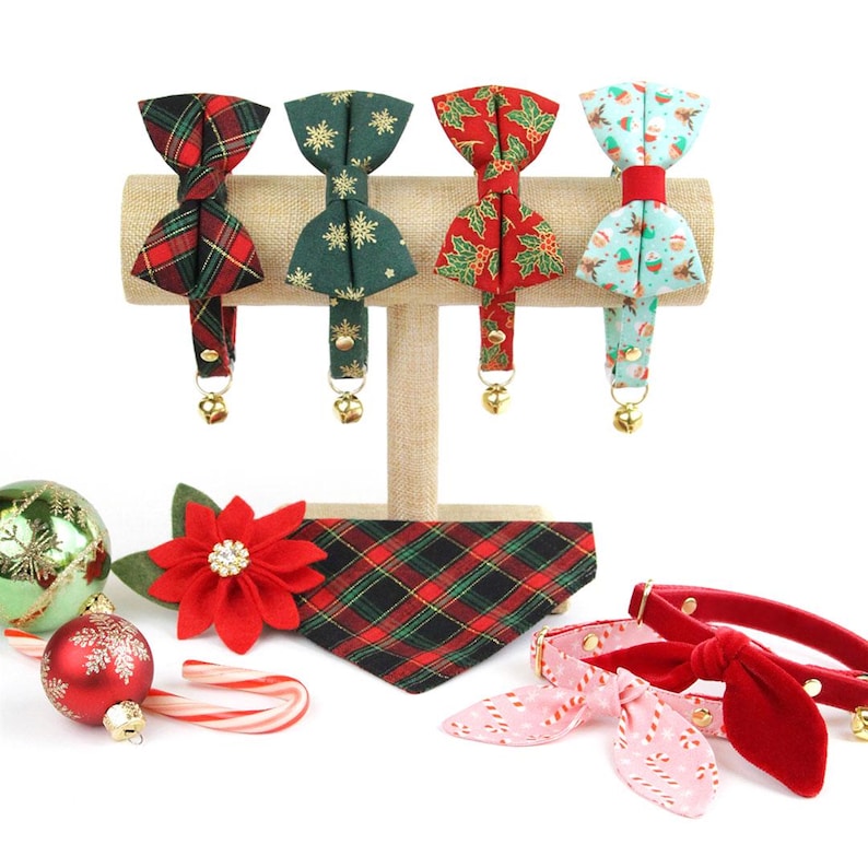 May include: A set of five festive Christmas-themed cat collars and bandanas. The collars feature a variety of patterns, including plaid, snowflakes, holly, and a snowman design. The bandanas are red and green plaid and red velvet with a pink and white candy cane pattern.