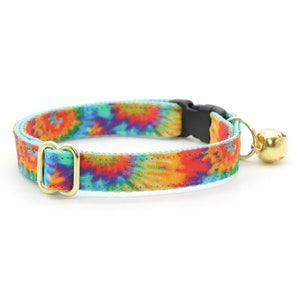 Może przedstawiać: Kolorowy kotek z krawatem w stylu tie-dye z złotą klamrą i złotym dzwonkiem. Kołnierz wykonany jest z miękkiej, wygodnej tkaniny i idealnie nadaje się dla kot&oacute;w w każdym rozmiarze.