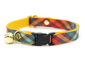 Puede incluir: Un collar para gato amarillo y a cuadros con una campana y una hebilla negra.